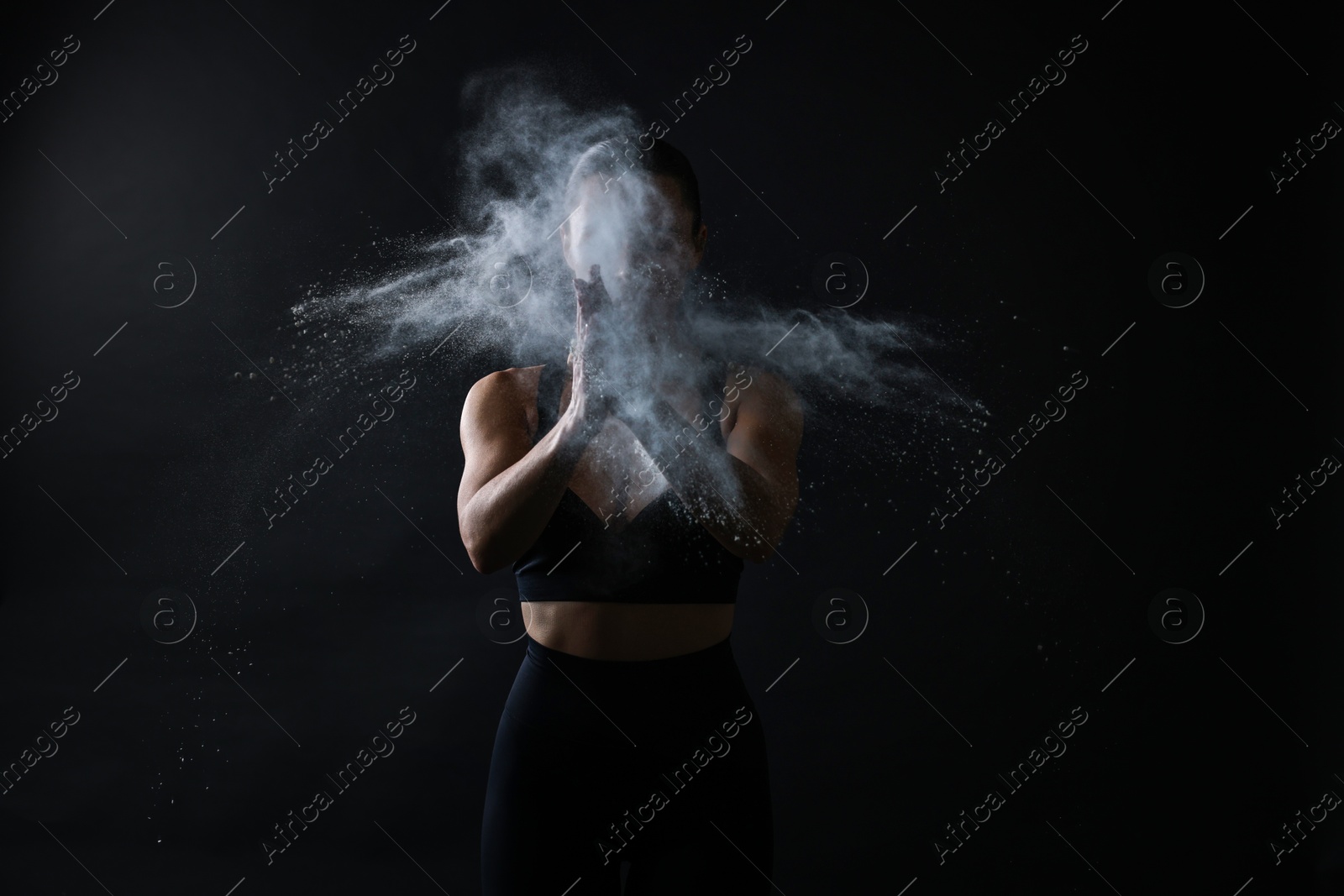 Photo of Woman clapping hands with talcum powder before training on black background