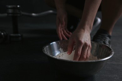 Photo of Woman applying talcum powder onto her hands above bowl before training in gym, closeup