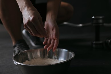 Photo of Woman applying talcum powder onto her hands above bowl before training in gym, closeup