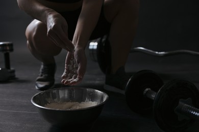 Photo of Woman applying talcum powder onto her hands above bowl before training in gym, closeup