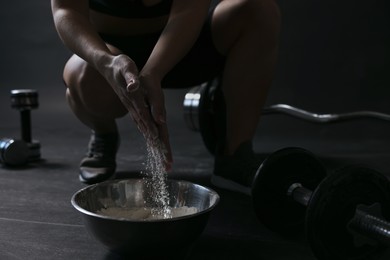 Photo of Woman applying talcum powder onto her hands above bowl before training in gym, closeup