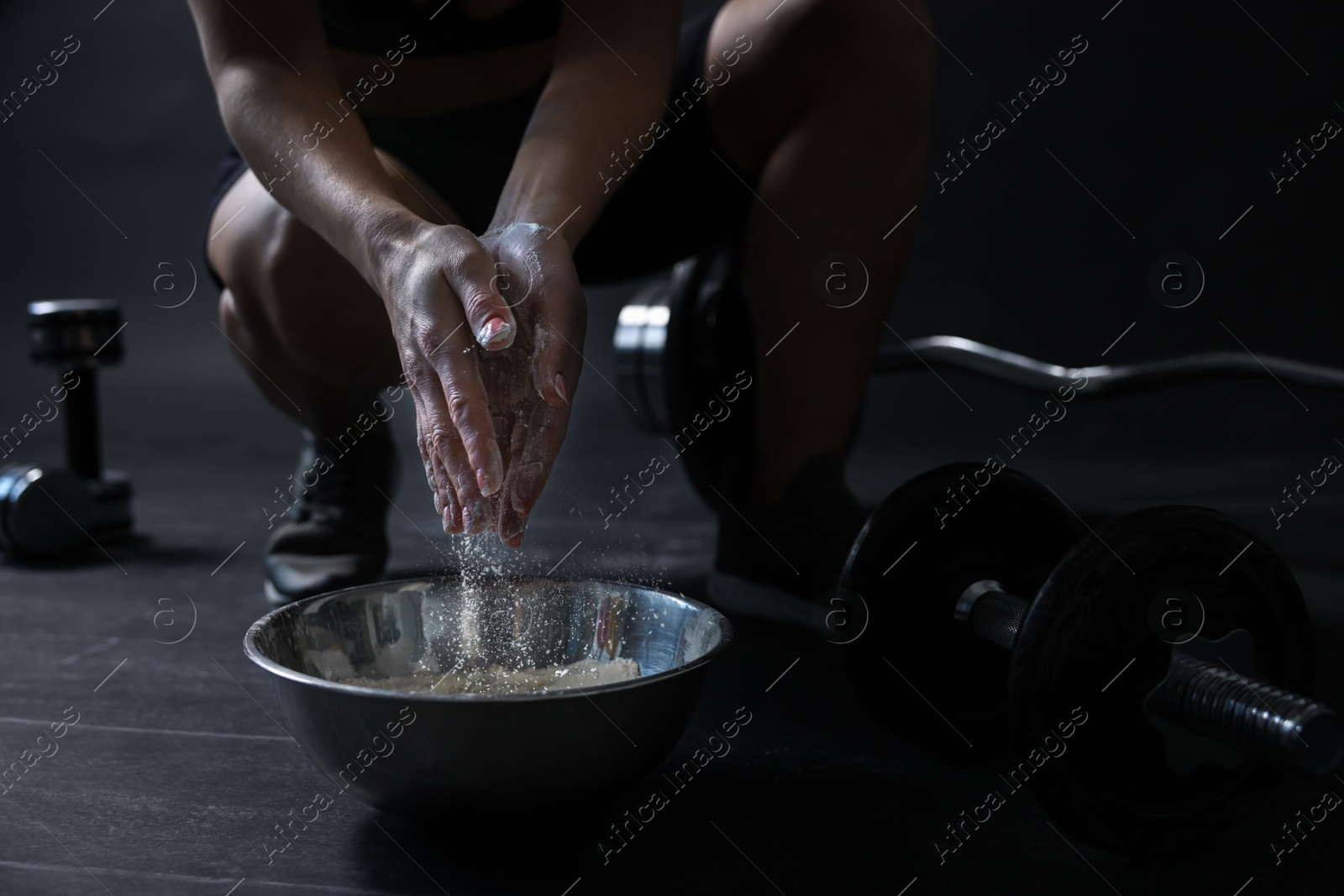 Photo of Woman applying talcum powder onto her hands above bowl before training in gym, closeup