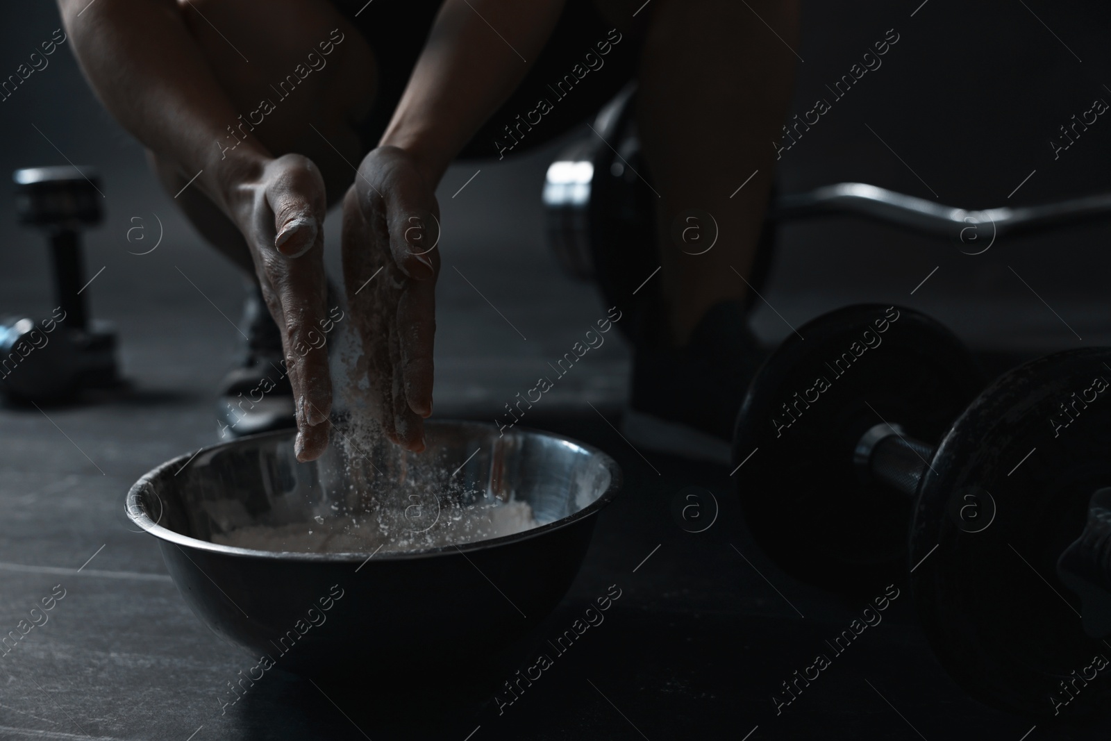 Photo of Woman applying talcum powder onto her hands above bowl before training in gym, closeup