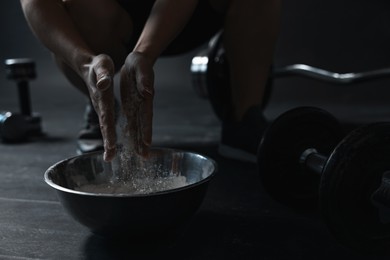 Photo of Woman applying talcum powder onto her hands above bowl before training in gym, closeup