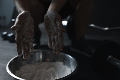 Photo of Woman applying talcum powder onto her hands above bowl before training in gym, closeup