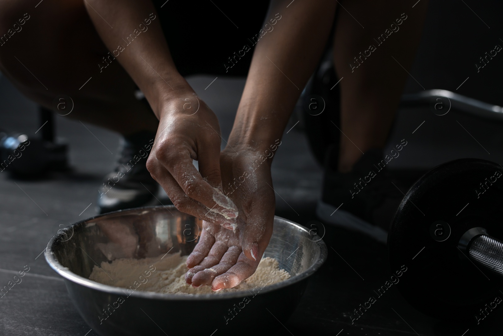 Photo of Woman applying talcum powder onto her hands above bowl before training in gym, closeup