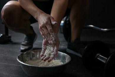 Photo of Woman applying talcum powder onto her hands above bowl before training in gym, closeup