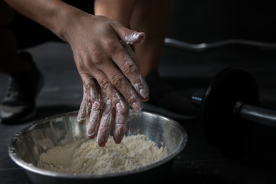 Photo of Woman applying talcum powder onto her hands above bowl before training in gym, closeup