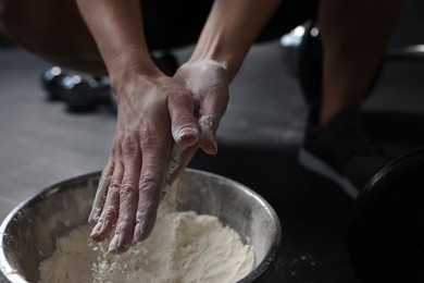 Photo of Woman applying talcum powder onto her hands above bowl before training in gym, closeup