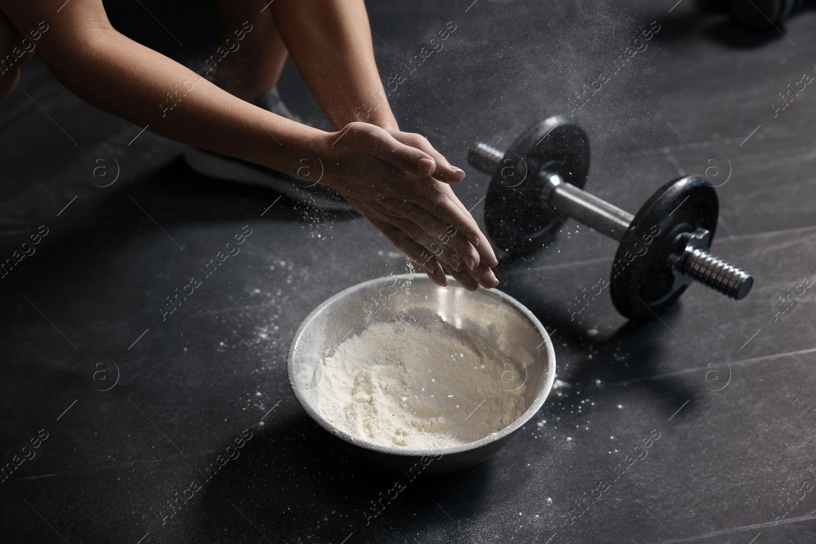 Photo of Woman clapping hands with talcum powder above bowl before training in gym, closeup