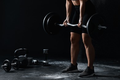 Photo of Woman with talcum powder on her hands training with barbell against black background, closeup