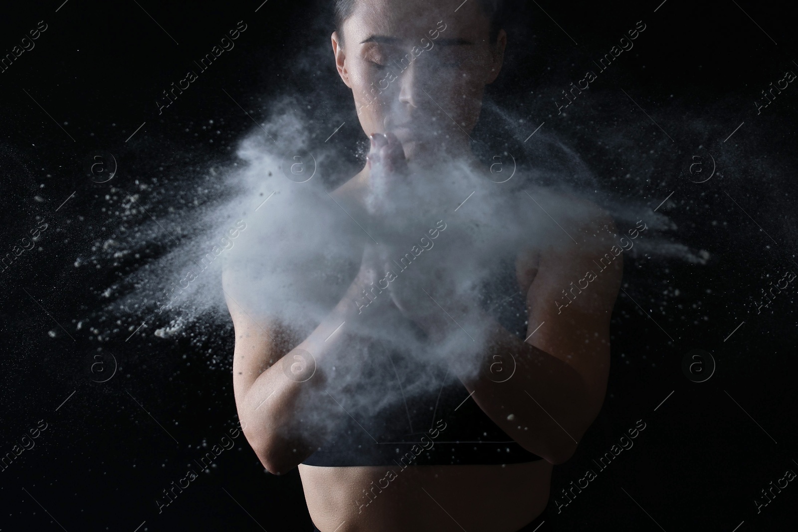 Photo of Woman clapping hands with talcum powder before training on black background