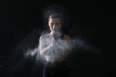 Photo of Woman clapping hands with talcum powder before training on black background