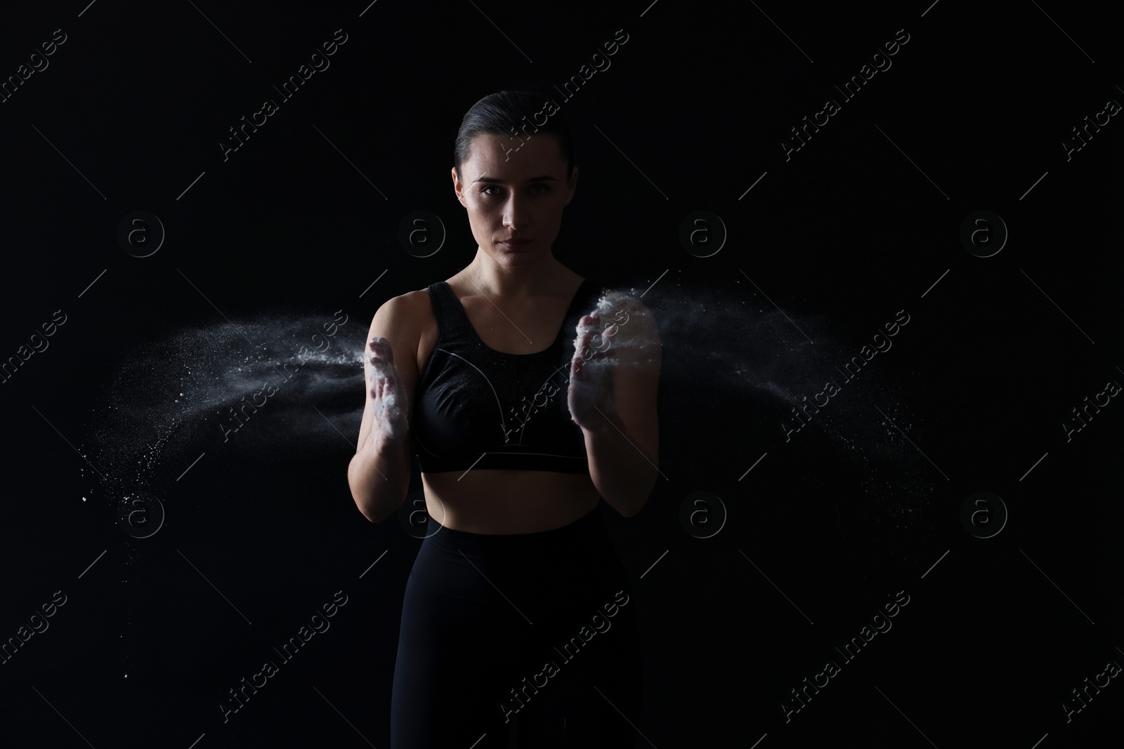 Photo of Woman clapping hands with talcum powder before training on black background