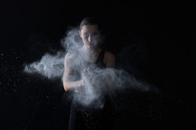 Photo of Woman clapping hands with talcum powder before training on black background