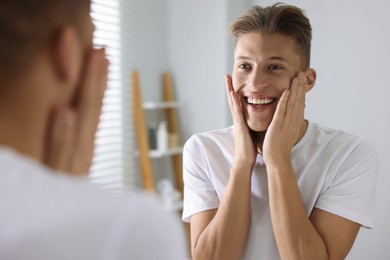 Photo of Washing face. Happy man looking at mirror in bathroom