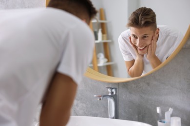 Photo of Washing face. Happy man looking at mirror in bathroom