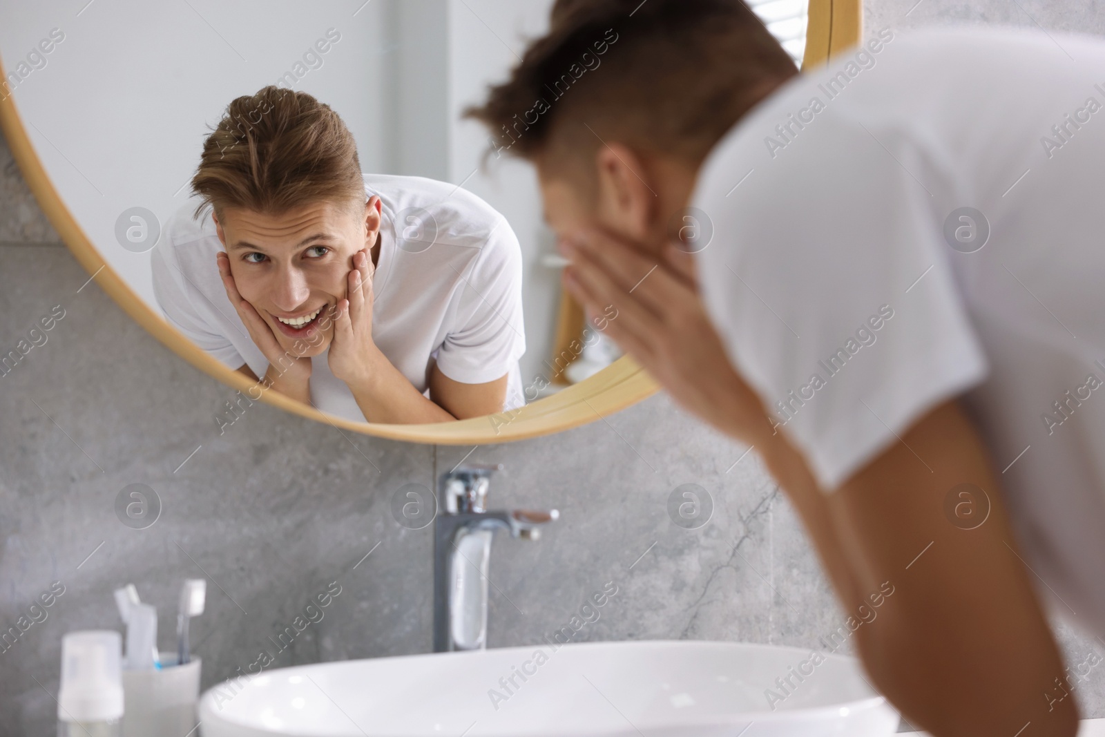 Photo of Washing face. Happy man looking at mirror in bathroom