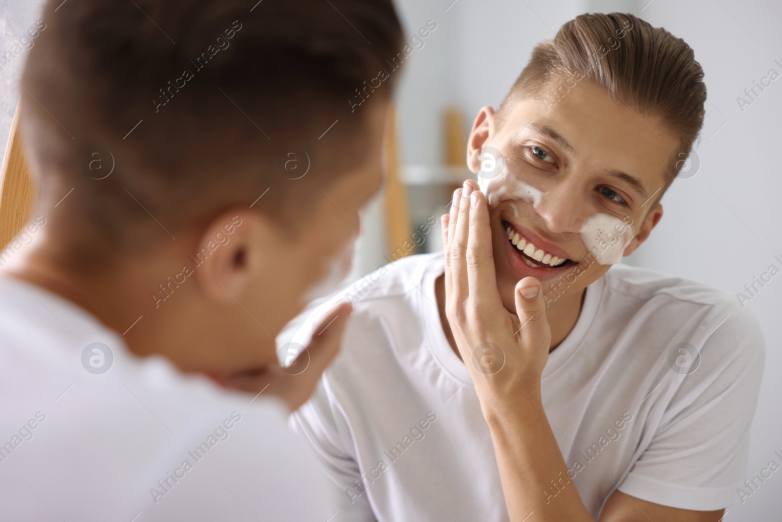 Photo of Man washing his face with cosmetic product near mirror in bathroom