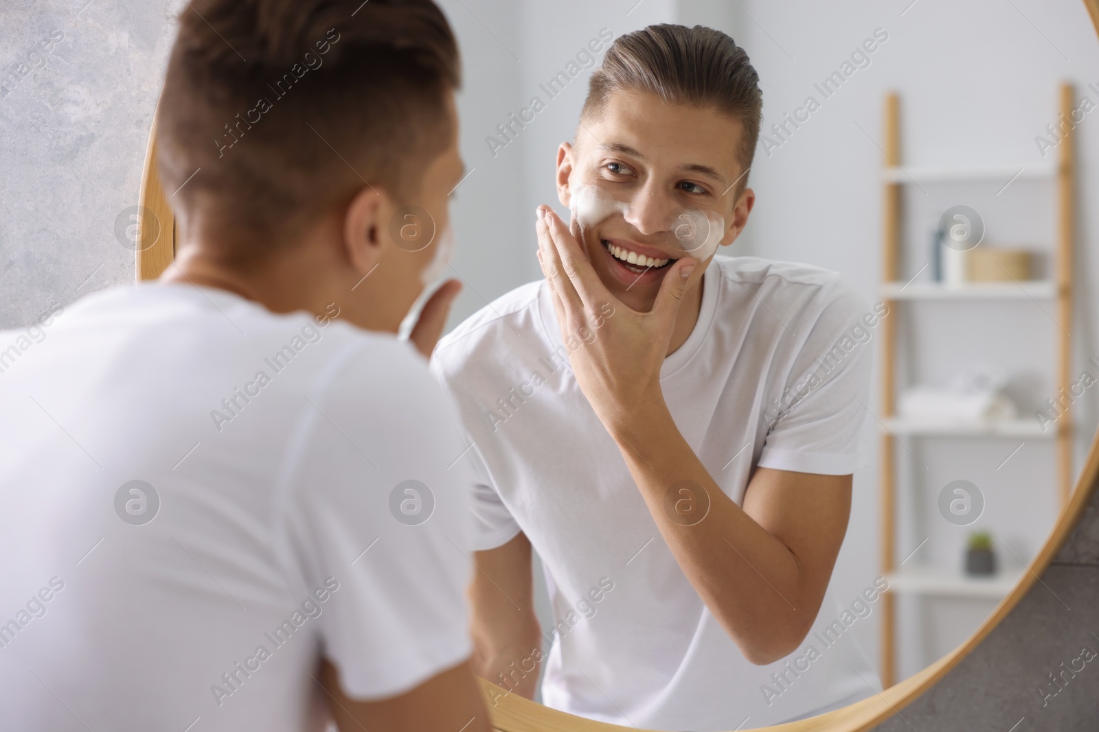 Photo of Man washing his face with cosmetic product near mirror in bathroom