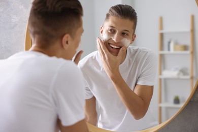 Photo of Man washing his face with cosmetic product near mirror in bathroom