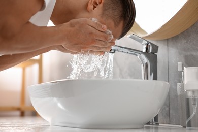 Photo of Man washing his face over sink in bathroom