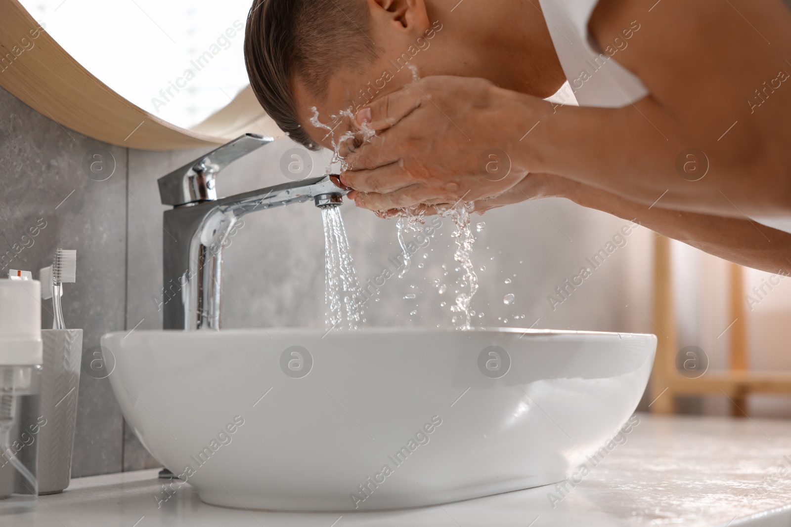 Photo of Man washing his face over sink in bathroom