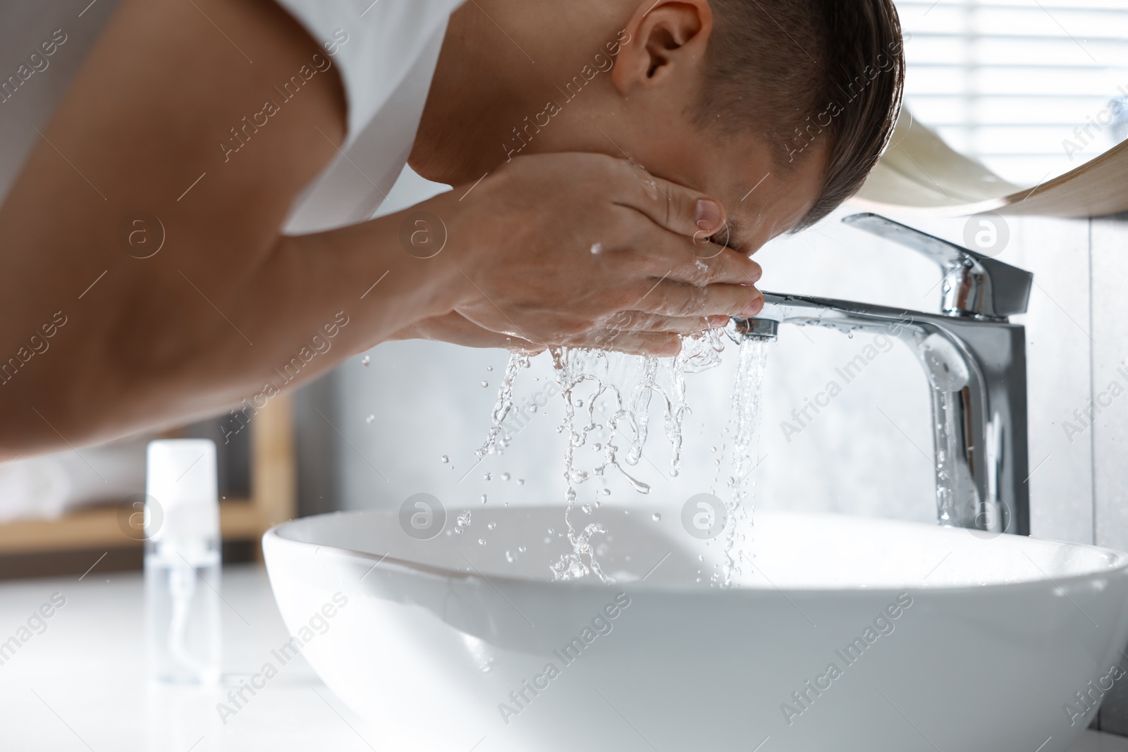 Photo of Man washing his face over sink in bathroom