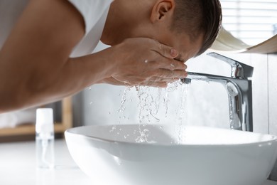 Photo of Man washing his face over sink in bathroom