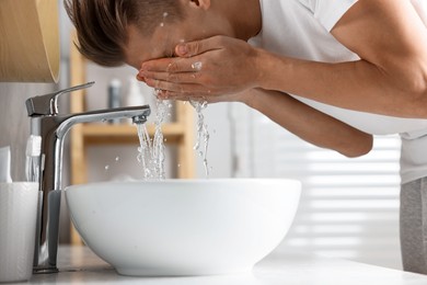 Photo of Man washing his face over sink in bathroom