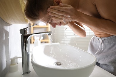 Photo of Man washing his face over sink in bathroom