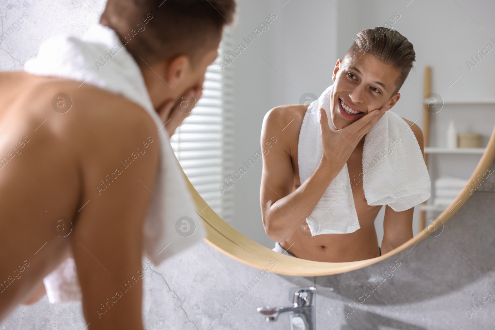 Photo of Washing face. Happy man looking at mirror in bathroom