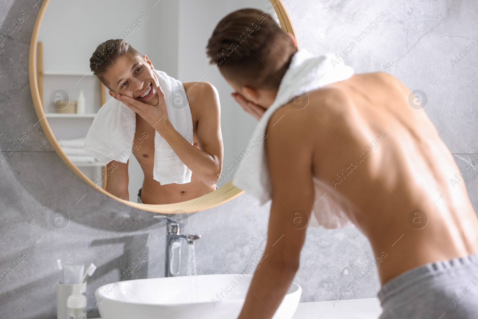 Photo of Washing face. Happy man looking at mirror in bathroom