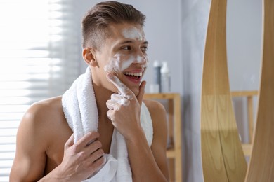 Photo of Man washing his face with cosmetic product near mirror in bathroom