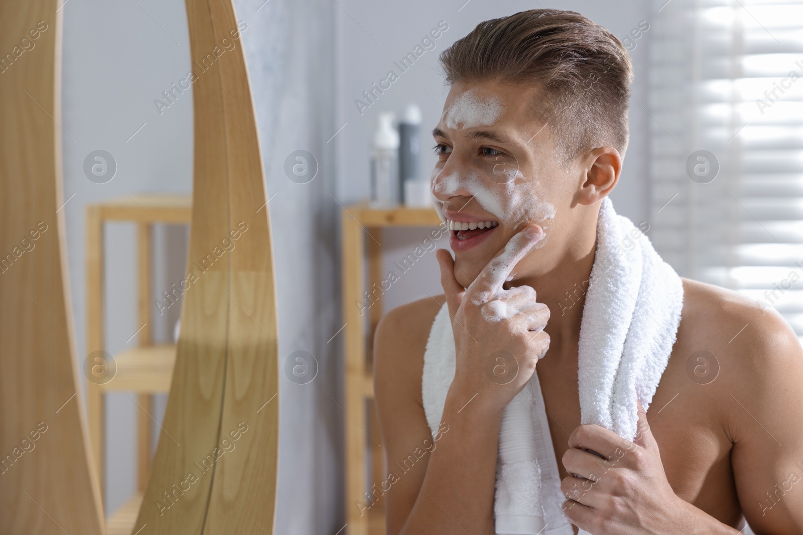 Photo of Man washing his face with cosmetic product near mirror in bathroom