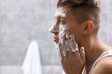 Photo of Man washing his face with cosmetic product in bathroom, space for text