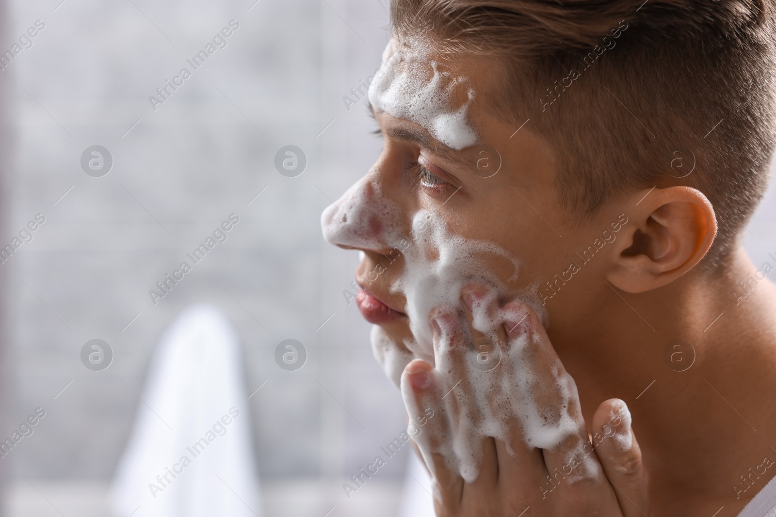 Photo of Man washing his face with cosmetic product in bathroom, space for text