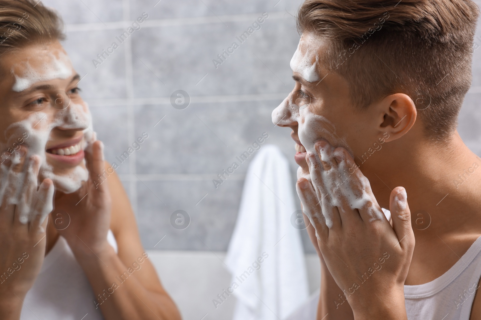 Photo of Man washing his face with cosmetic product near mirror in bathroom