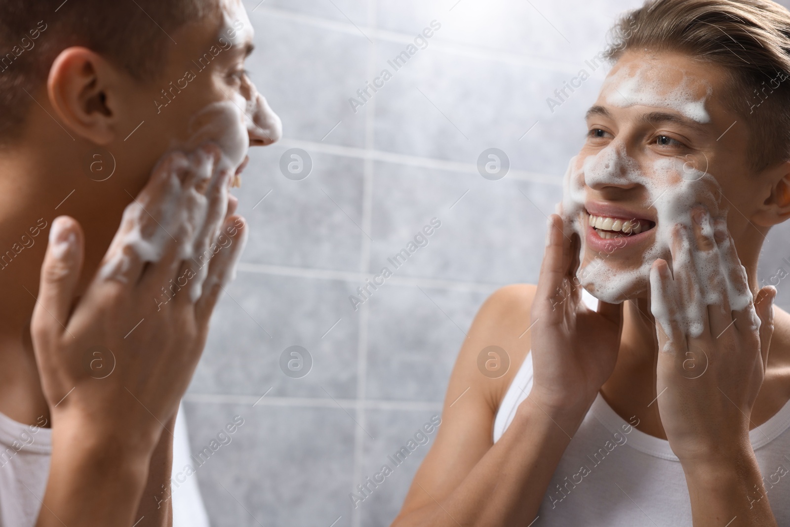 Photo of Man washing his face with cosmetic product near mirror in bathroom