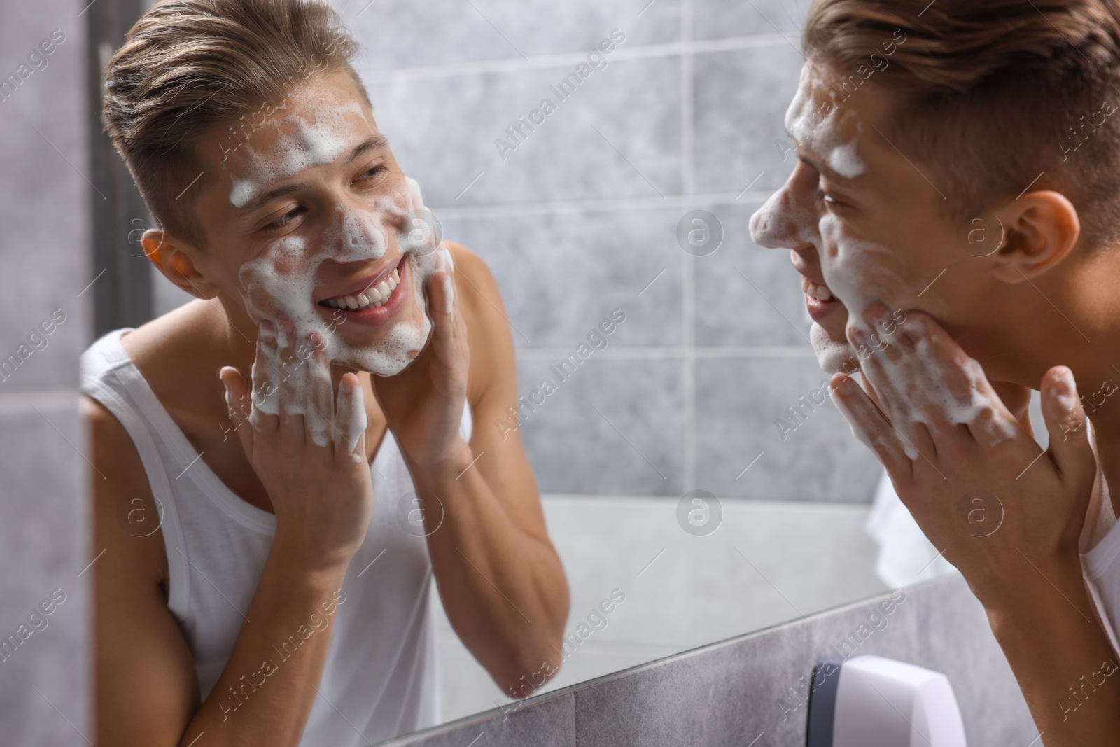 Photo of Man washing his face with cosmetic product near mirror in bathroom