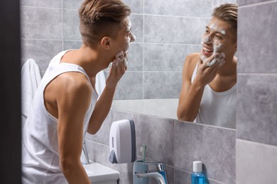 Photo of Man washing his face with cosmetic product near mirror in bathroom