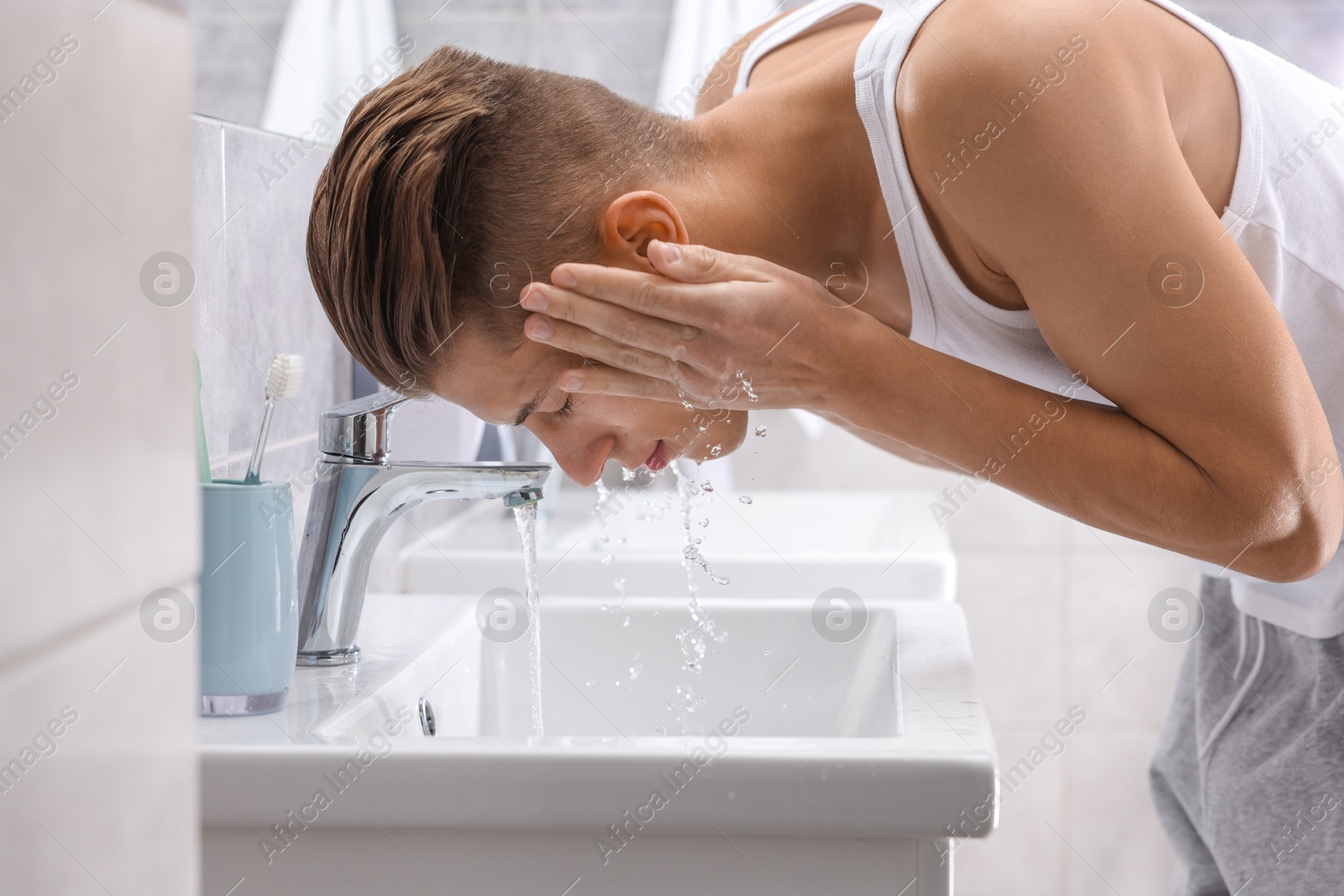 Photo of Man washing his face over sink in bathroom