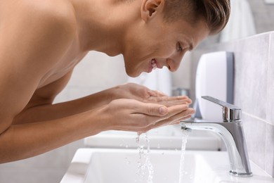 Photo of Happy man washing his face over sink in bathroom