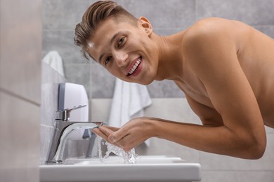 Photo of Happy man washing his face over sink in bathroom