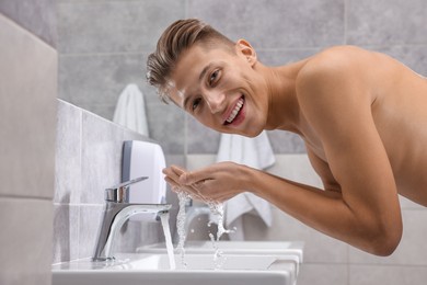 Photo of Happy man washing his face over sink in bathroom