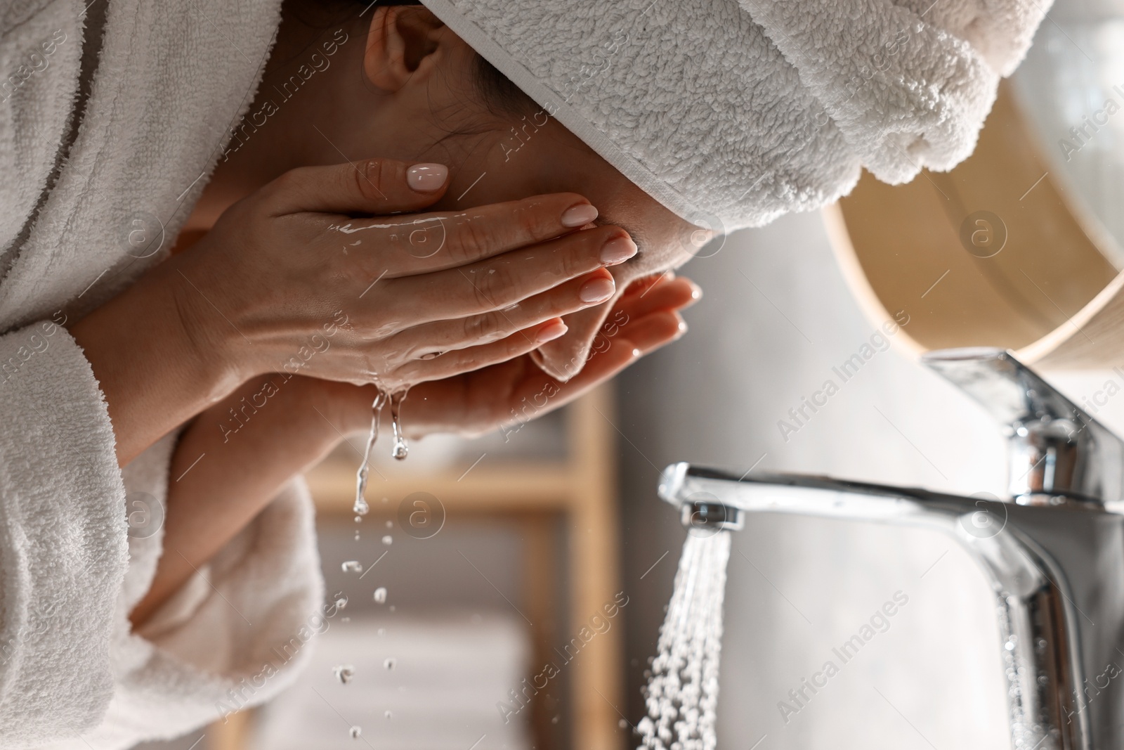 Photo of Woman in bathrobe washing her face in bathroom