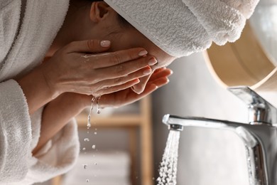 Photo of Woman in bathrobe washing her face in bathroom