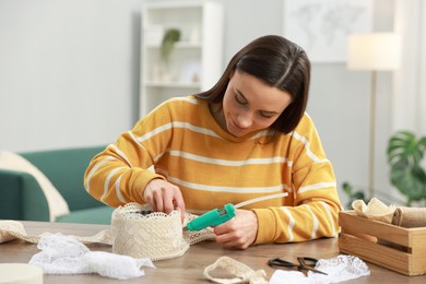 Photo of Woman with hot glue gun making craft at table indoors