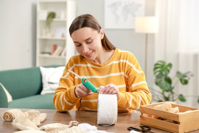 Photo of Woman with hot glue gun making craft at table indoors