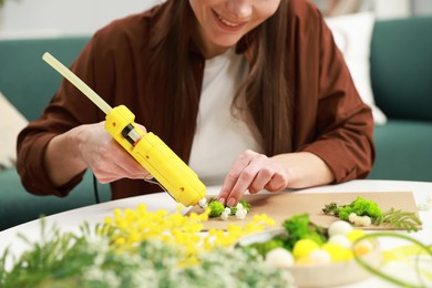 Photo of Woman with hot glue gun making craft at table indoors, closeup